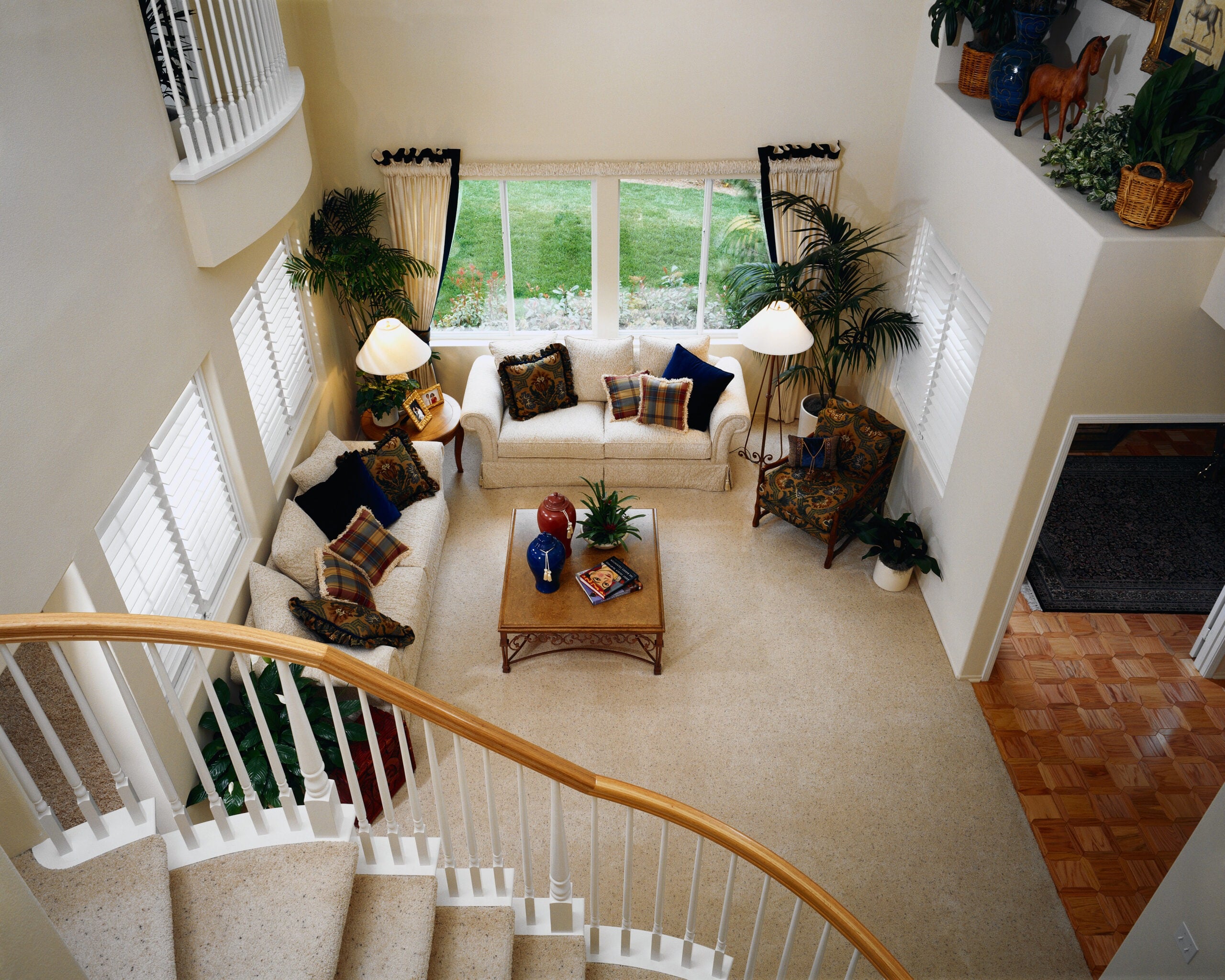 Living room view from stairs featuring a cozy arrangement of white sofas, decorative pillows, a wooden coffee table, indoor plants, and a lamp, showcasing a clean and inviting space ideal for family gatherings.
